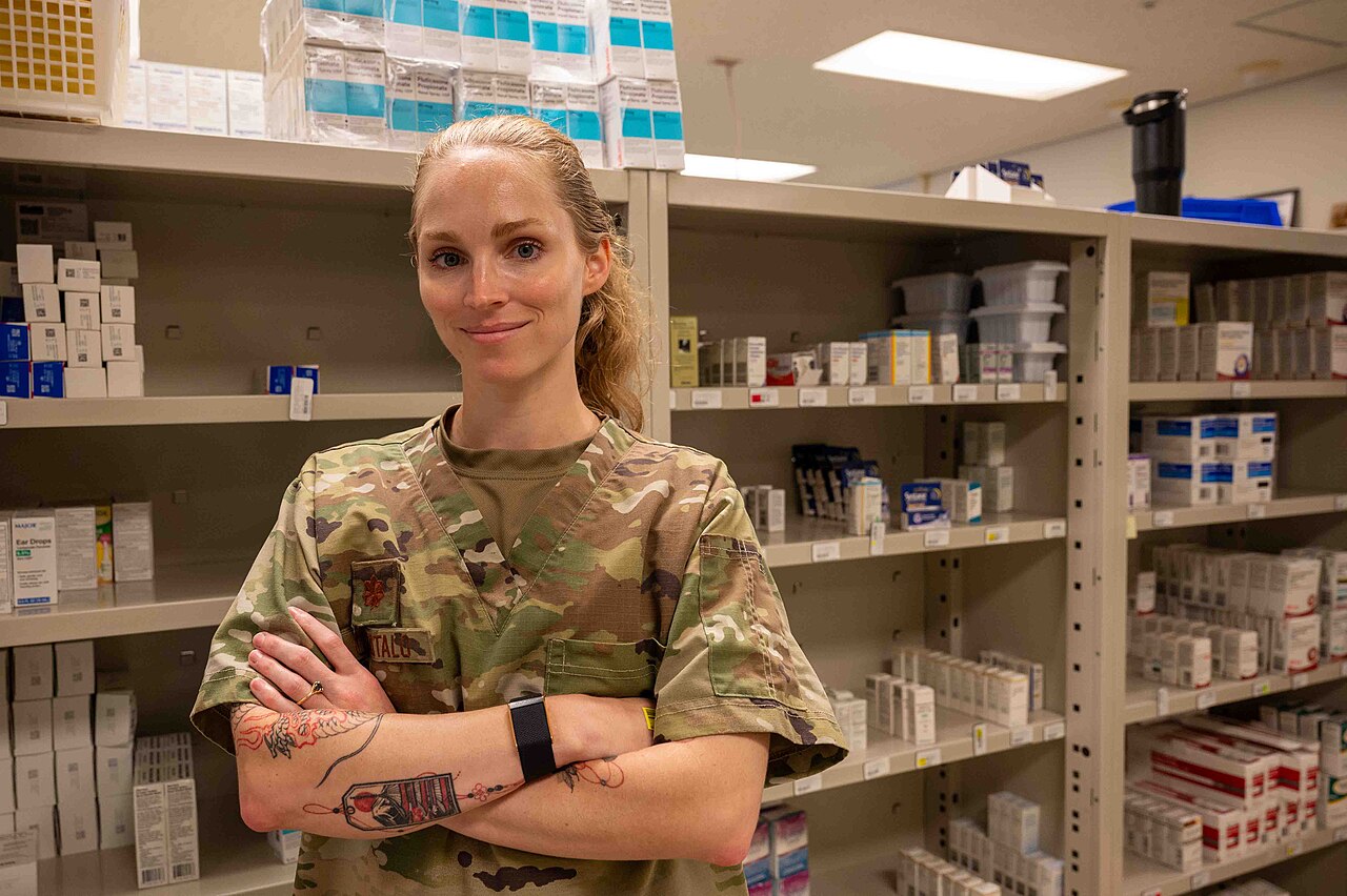 A U.S. Air Force pharmacy officer standing in a military treatment facility pharmacy stocked with prescription medications